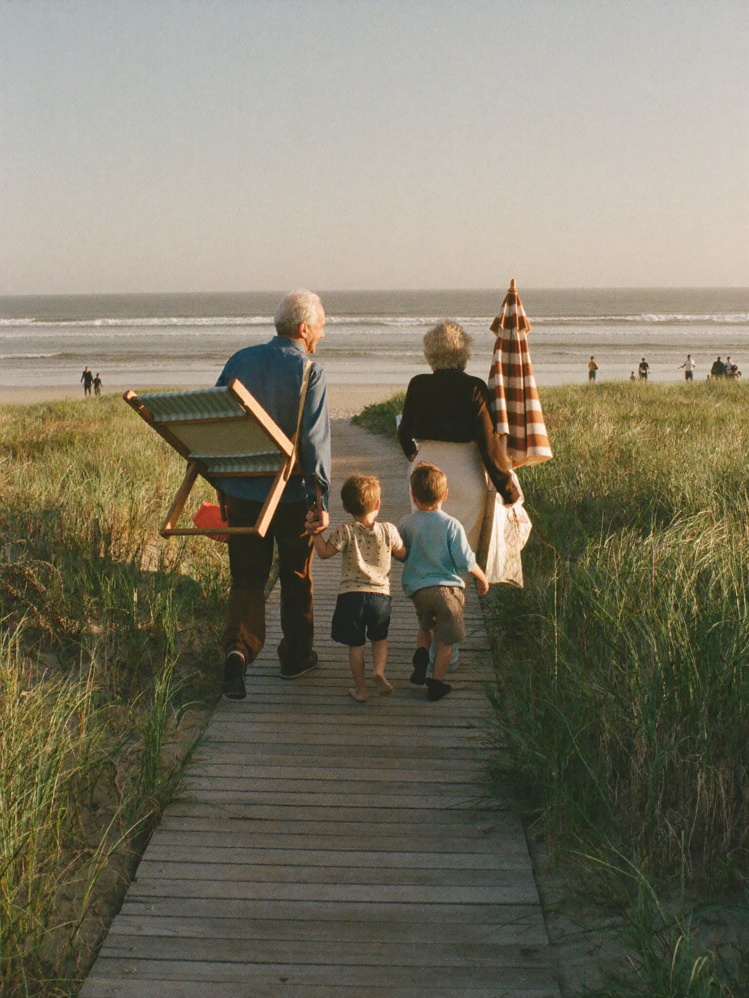Grandparents walking two kids down a dune boardwalk to the beach at golden hour